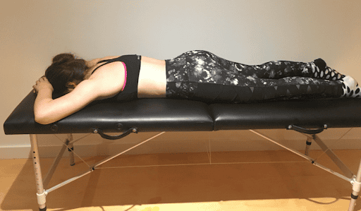 Woman performing a back stretch exercise on a treatment table for low back pain relief.