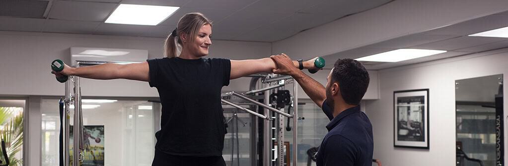 Woman performing strength exercise with trainer in physiotherapy clinic.