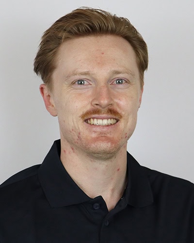 Portrait of a smiling man with red hair and fair skin in a black polo shirt.