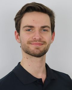 Portrait of a young man with brown hair and a beard, smiling at the camera.